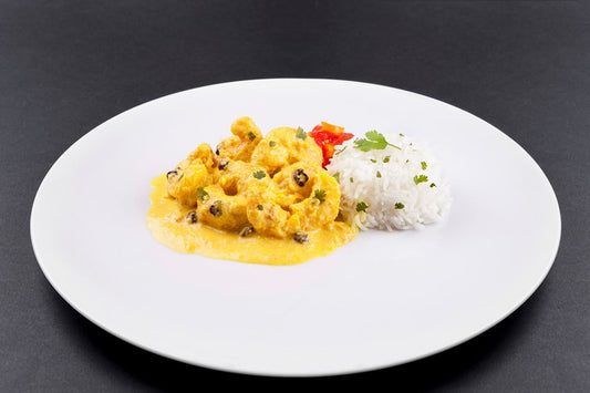 Coconut Prawn Korma, the finished product on a white plate with white boiled rice and a fresh tomato chutney. There are sultanas and fresh coriander spinkled on top of the finished dish.